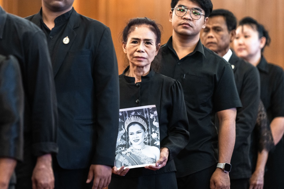 A mourner holds a portrait of Thailand’s former Queen Sirikit while lining up to pay respects to the late queen at the Grand Palace in Bangkok on October 26, 2025. The year-long funeral ceremony of Thailand’s former Queen Sirikit started on October 26, with grieving royalists set to salute the procession bringing her remains to lie in state at Bangkok’s Grand Palace. (Photo by Chanakarn Laosarakham / AFP)